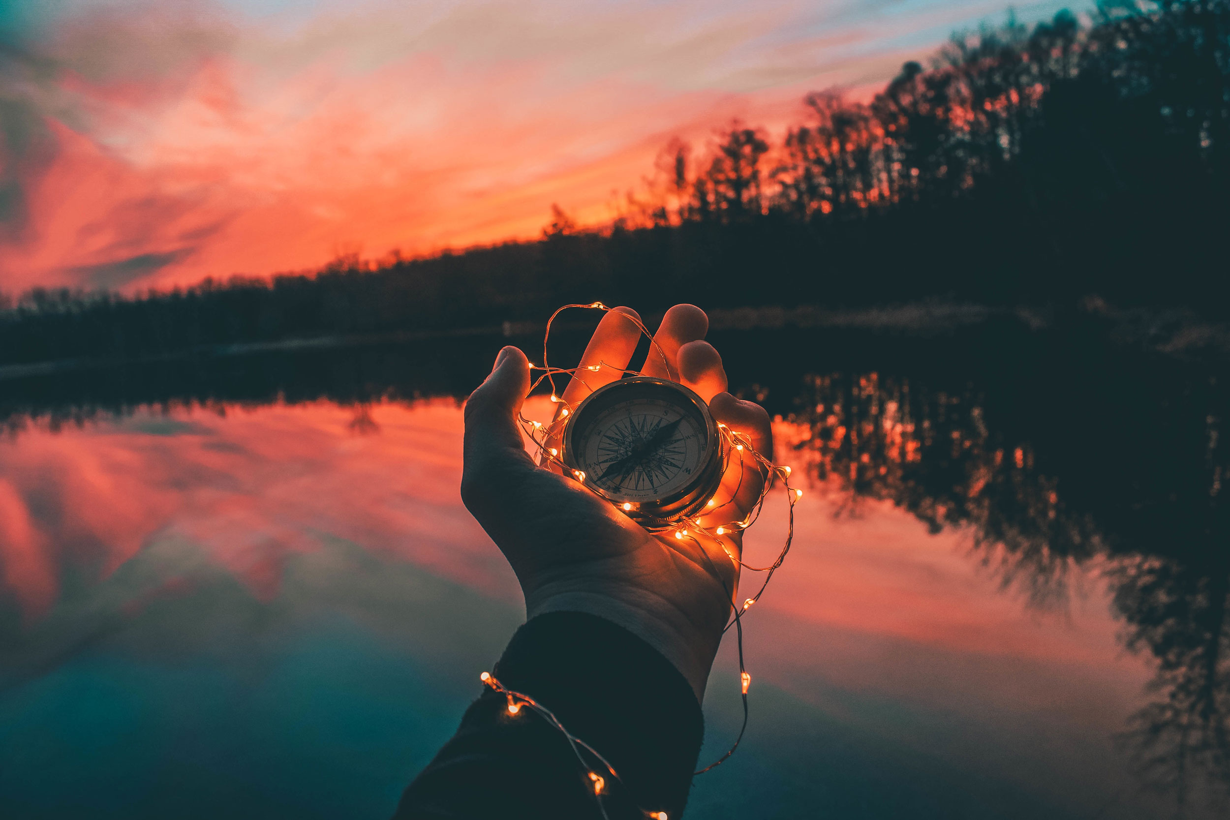 Kompass in einer Hand mit Lichterkette vor einem See im Abendlicht